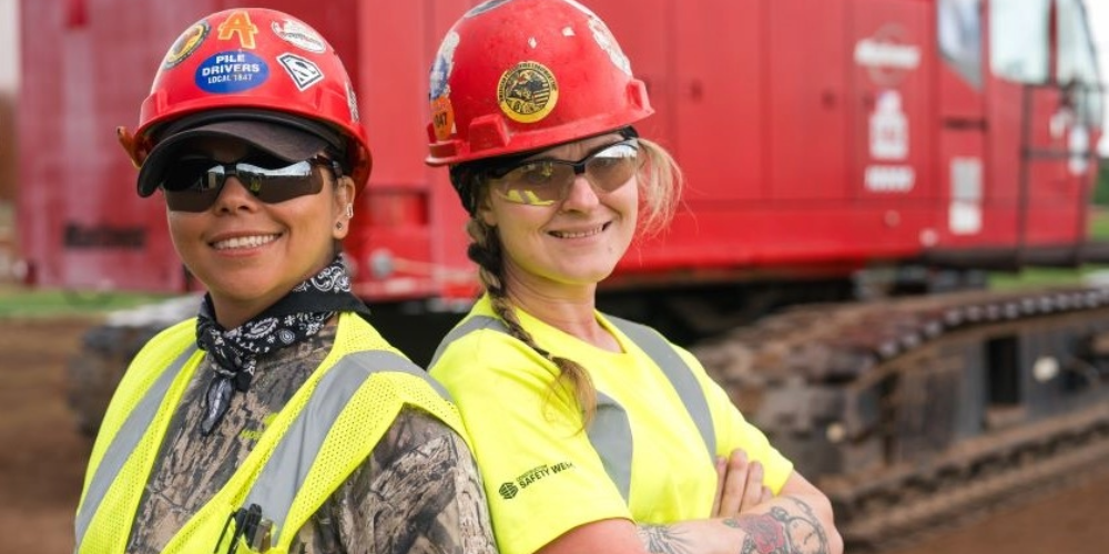 Two workers in green safety vests and hard hats.